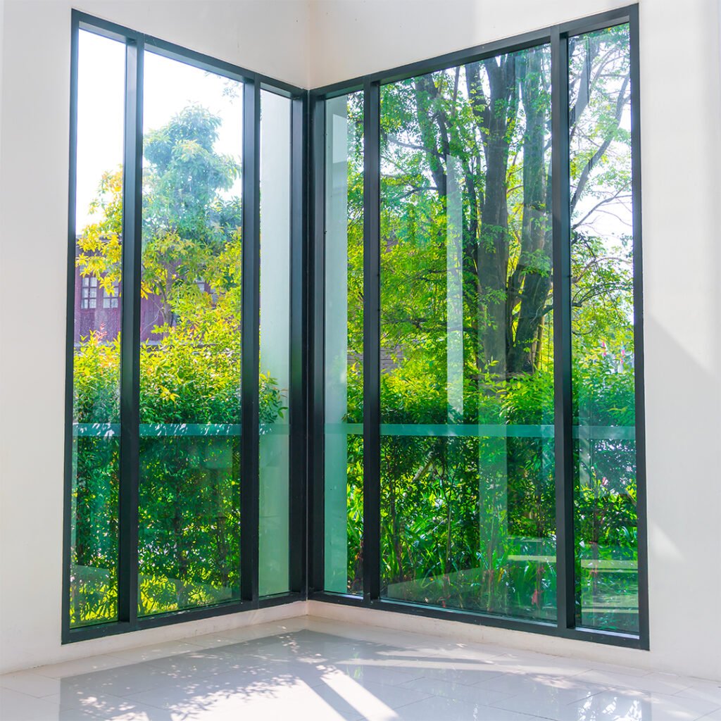 Duas janelas de vidro em um sala branca com a vista para um jardim verde.